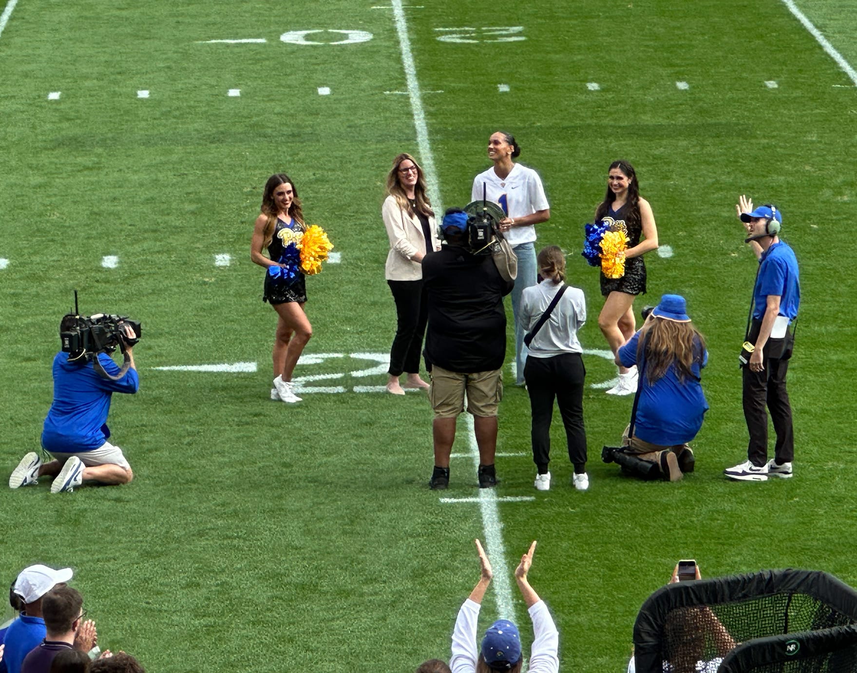 Cheerleaders standing with a Pitt administrator and Olivia Babcock on the grass at Acrisure Stadium