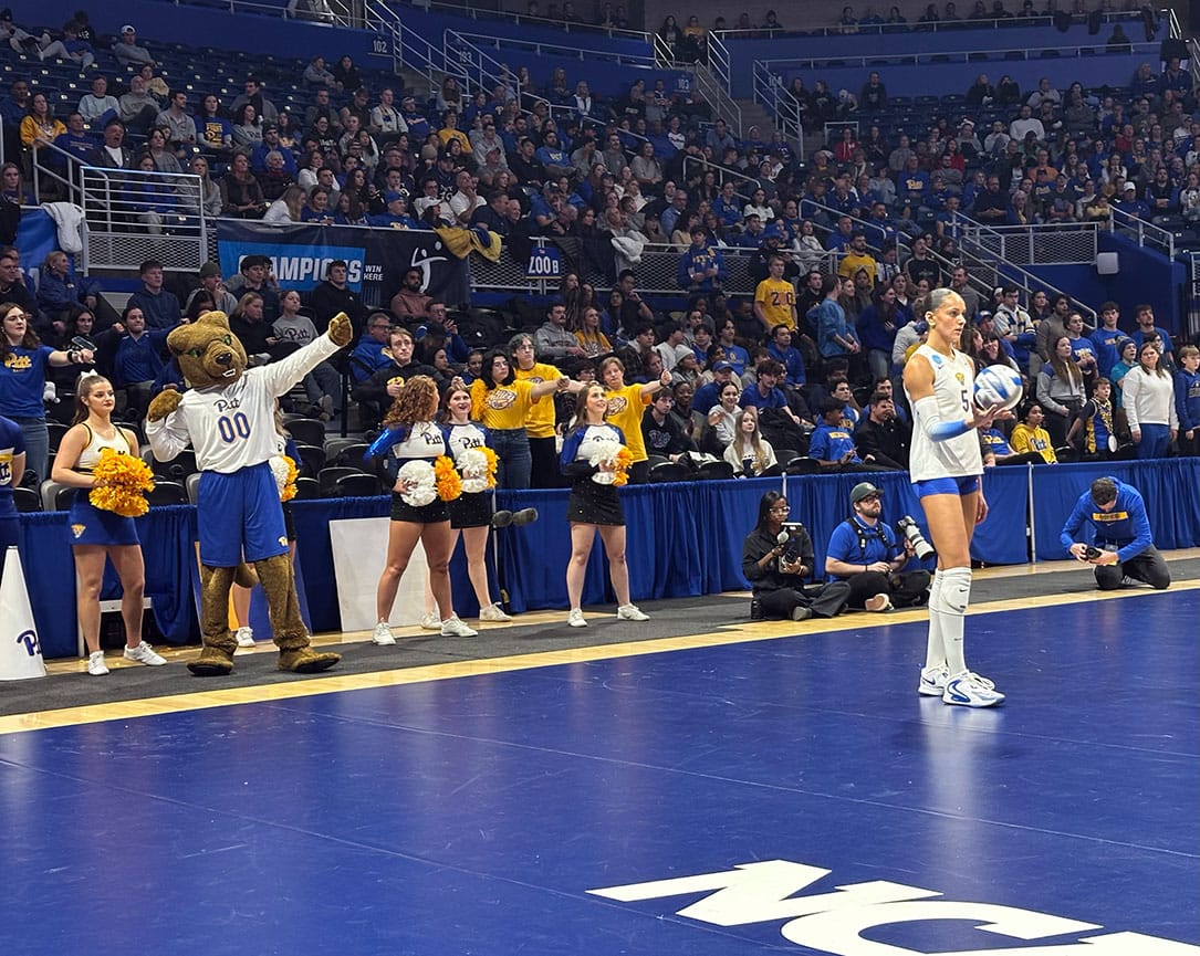 Olivia Babcock prepares to serve with Roc the Panther and the Pitt band behind her