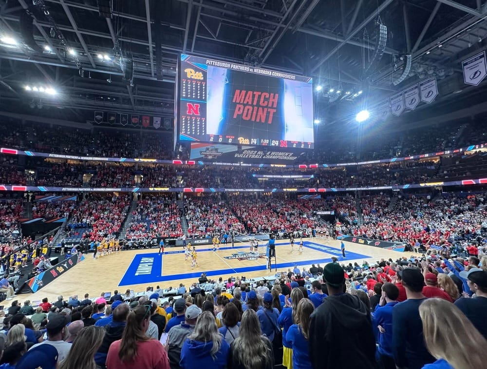 A view from the seating bowl of Amalie Arena in Tampa during match point of the 2023 Women's Volleyball Final Four. There are many fans looked toward a volleyball court.