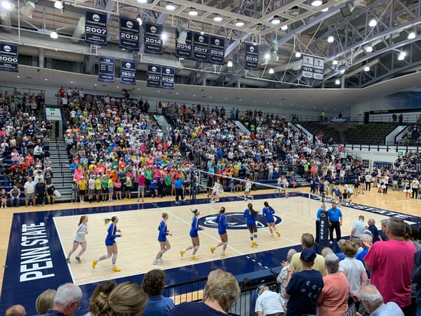 A 2019 photo inside the Rec Hall volleyball arena at Penn State, showing a sold out crowd and players warming up on the court before first serve