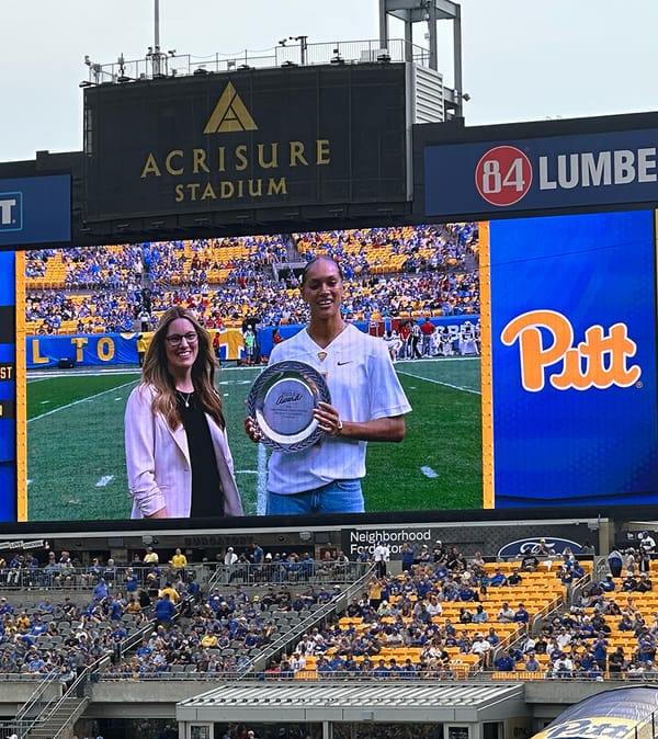 Okay, the photo shows Pitt Volleyball's Olivia Babcock holding a silver plate for the Honda Award for volleyball, seen on a stadium scoreboard