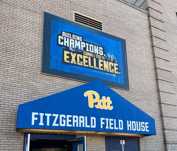 Photo shows the yellow brick exterior of the Fitzgerald Field House with a sign above that says Building Champions - Committed to Excellence