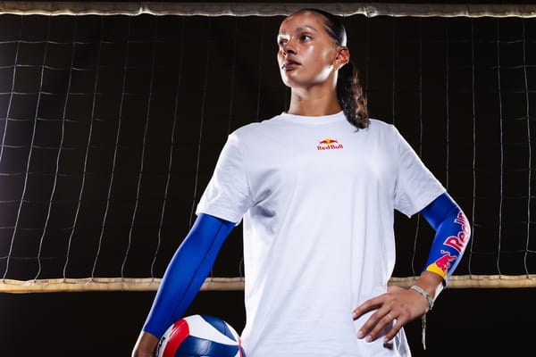 Olivia Babcock standing in a heroic pose in front of a volleyball net while wearing Red Bull gear